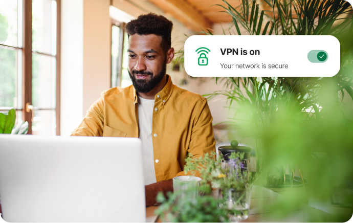 植物に囲まれた男性が微笑みながらノートパソコンを見ている